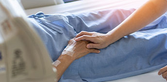 Caregiver Holding Senior Patient Hand In Hospital Bed
