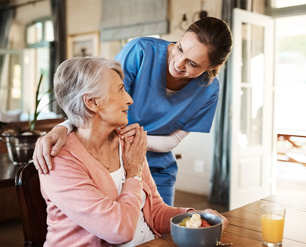 Elderly Woman With Nurse Eating Breakfast At The Table