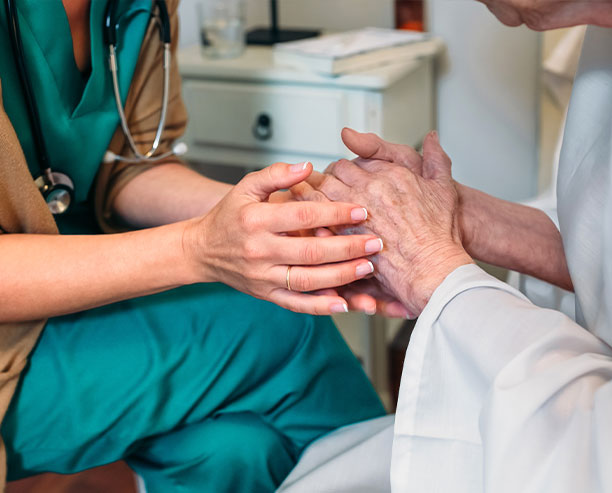 Female Doctor Giving Encouragement To Elderly Patient By Holding Her Hands