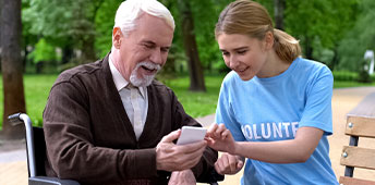 Female Volunteer Helping Disabled Old Man Use Smartphone