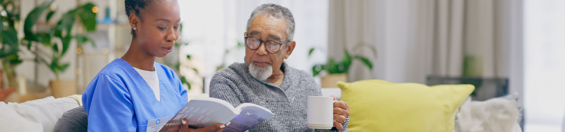 Senior Man Drinking From Mug With Volunteer In Hospice For Rehabilitation