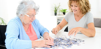 Woman Doing Puzzle And Spending Time With Elderly Senior